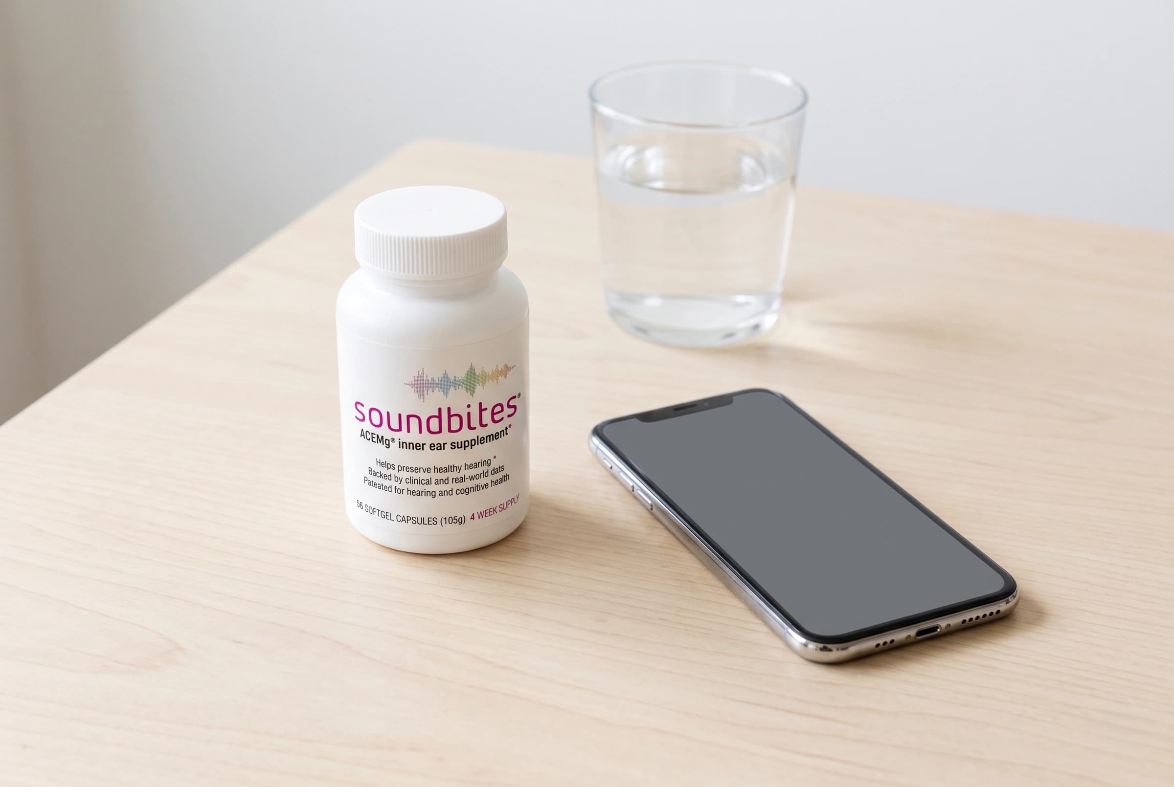 A bottle of Soundbites ACEMg on a desk beside a phone and a glass of water: the daily softgel and the way to measure it