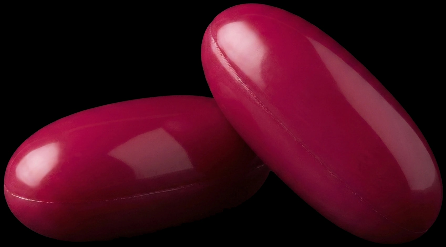A single deep-raspberry Soundbites ACEMg softgel capsule, lit against a dark teal background